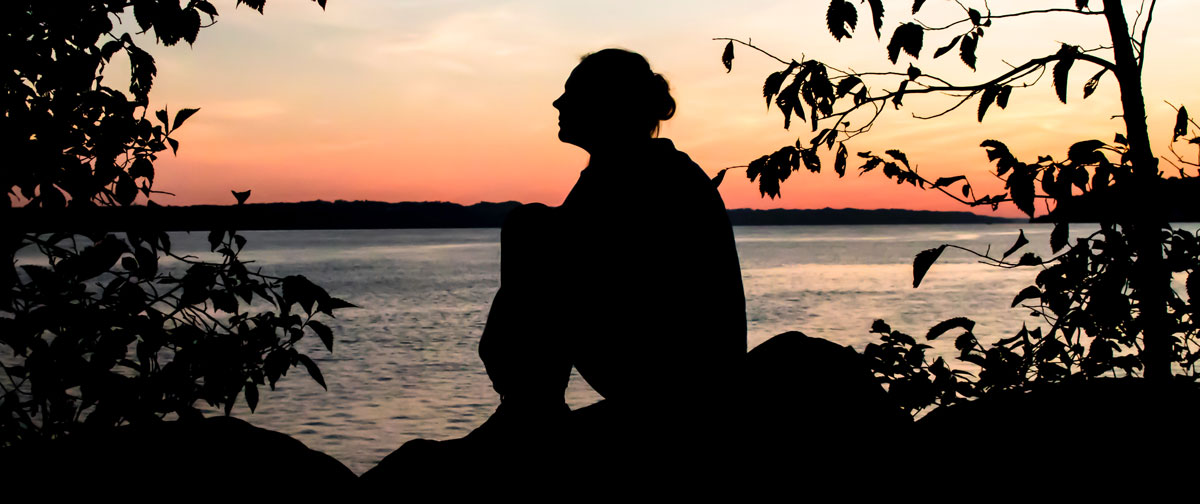 Woman that experienced domestic violence sitting down beside a lake during sunset